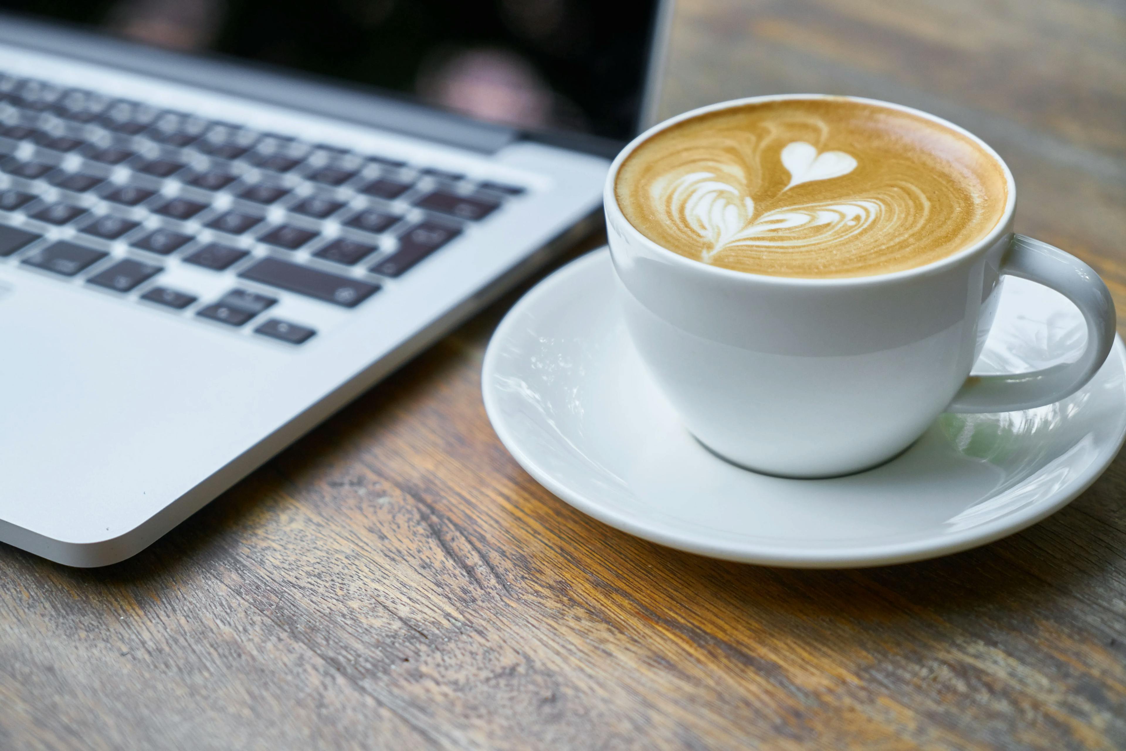 Nærbilde av Macbook med en kaffekopp ved siden av.
